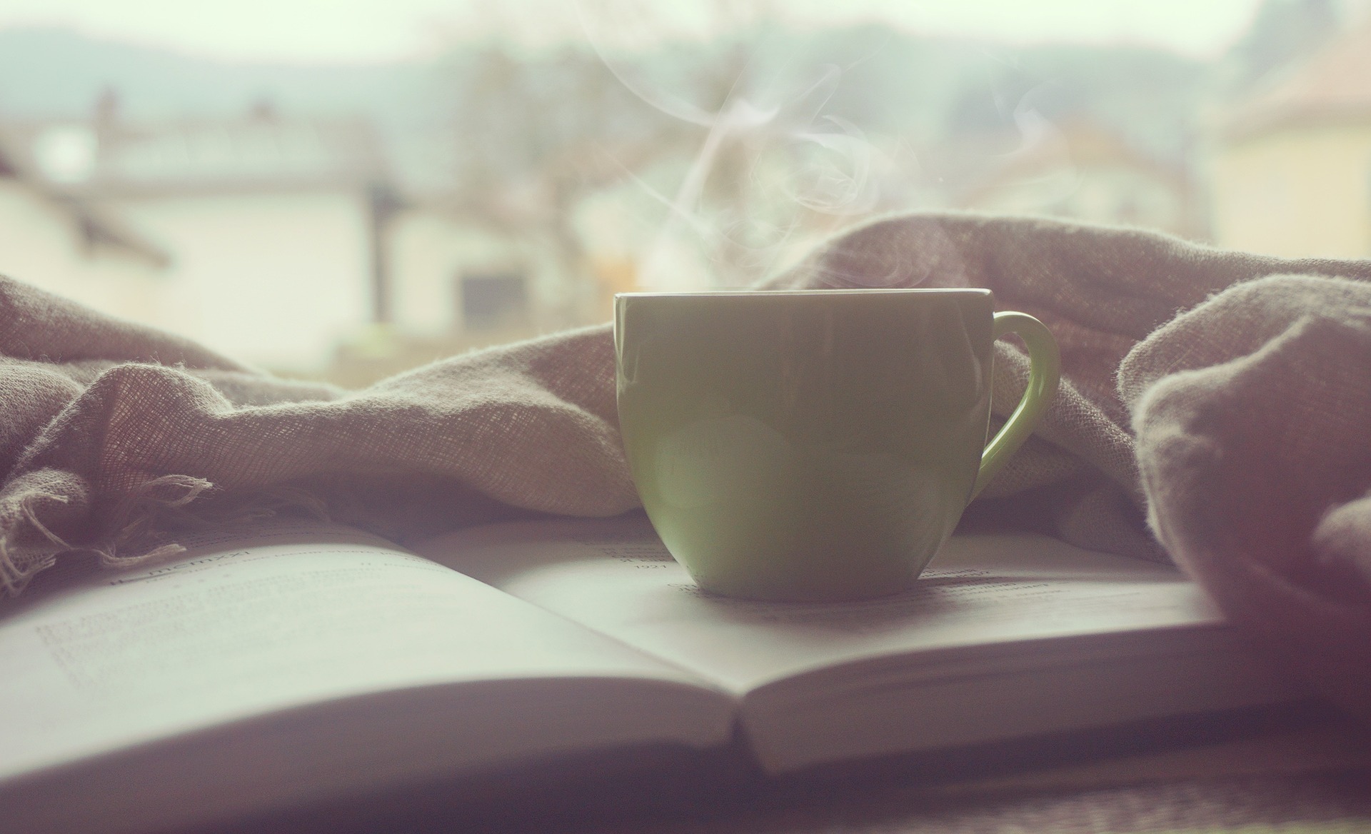 A cup of coffee resting on a journal, both sitting on a bed with a blanket in the background